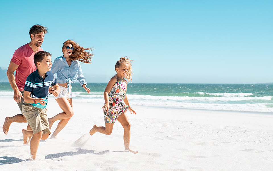 Familienurlaub Fr&uuml;hbucher: Familie l&auml;uft am Strand entlang im Familienurlaub