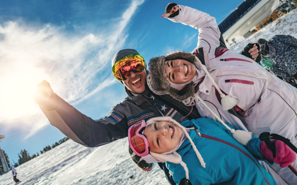 Familie im Skioutfit jubelt auf einer Skipiste bei strahlendem Sonnenschein
